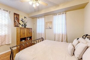 Un dormitorio con cama, armario de madera, cortinas y ventilador de techo.