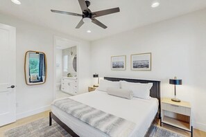 Ein Schlafzimmer mit Bett, Nachttischen, Deckenventilator, Spiegel und gerahmten Bildern an der Wand.