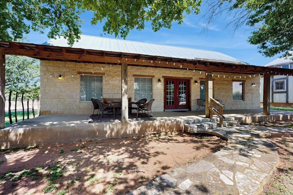 Un edificio de piedra con un porche cubierto, asientos al aire libre y una puerta roja.
