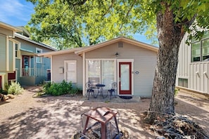 A small, single-story building with a front door, two windows, and a patio with a table and chairs. - Cozy Retreat in Fredericksburg - Two Homes Perfect for Large Groups (Fredericksburg)