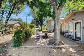 A residential area with a tree-lined driveway, a small patio with outdoor furniture, and a house with a garage. - Cozy Retreat in Fredericksburg - Two Homes Perfect for Large Groups (Fredericksburg)
