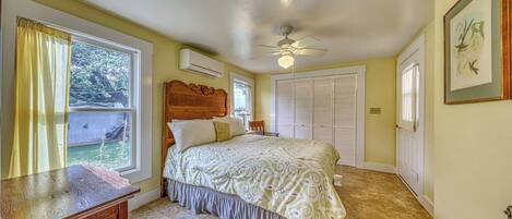 A bedroom with a bed, a ceiling fan, a window with curtains, a door, and a framed picture on the wall.