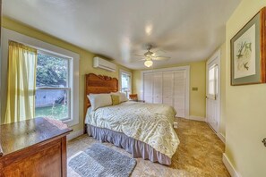 A bedroom with a bed, a ceiling fan, a window with curtains, a door, and a framed picture on the wall. - Historic Fredericksburg Farmhouse - Hill Country Views - Wine Trail - Snowbird (Fredericksburg)