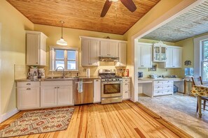 A kitchen with wooden flooring, white cabinets, a stove, and a ceiling fan. - Historic Fredericksburg Farmhouse - Hill Country Views - Wine Trail - Snowbird (Fredericksburg)