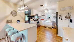 Una cocina moderna con armarios blancos, una isla central con taburetes altos, iluminación colgante y una lámpara decorativa.