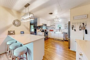 Cozinha moderna com armários brancos, ilha central com banquetas, iluminação pendente e luminária suspensa.