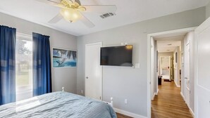 Quarto com cama, ventilador de teto, TV e corredor que dá para outros cômodos.