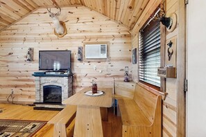 A log cabin interior with a stone fireplace, wooden benches, a television, and mounted animal heads. - Dog-friendly Gem on 11 Acres With Valley Views, Deck, Gas Grill, Fireplace (Fredericksburg)