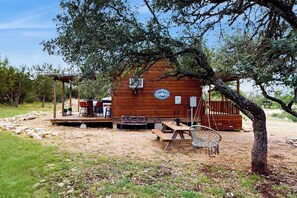 A rustic cabin with a wooden deck, outdoor seating, and a swing chair. - Dog-friendly Gem on 11 Acres With Valley Views, Deck, Gas Grill, Fireplace (Fredericksburg)
