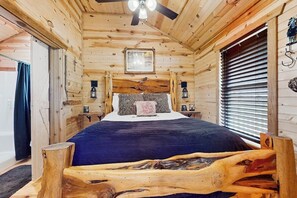 A wooden cabin bedroom with a bed, a ceiling fan, and a window with blinds. - Dog-friendly Gem on 11 Acres With Valley Views, Deck, Gas Grill, Fireplace (Fredericksburg)