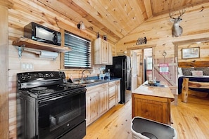 A wooden cabin interior with a kitchen featuring a stove, microwave, cabinets, and a refrigerator. - Dog-friendly Gem on 11 Acres With Valley Views, Deck, Gas Grill, Fireplace (Fredericksburg)