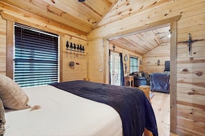 A wooden cabin interior with a bed, a small seating area, and a door leading outside. - Dog-friendly Gem on 11 Acres With Valley Views, Deck, Gas Grill, Fireplace (Fredericksburg)