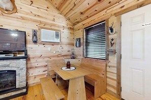 A wooden cabin interior with a stone fireplace, a dining table with benches, a television, and a door with a 'No Smoking' sign. - Dog-friendly Gem on 11 Acres With Valley Views, Deck, Gas Grill, Fireplace (Fredericksburg)