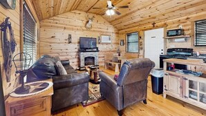 Ein Blockhaushaus-Interieur mit Kamin, Ledermöbeln, Deckenventilator und Küchenzeile.