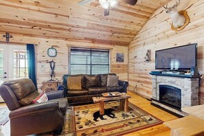 A log cabin interior with a leather sofa, a fireplace, a mounted deer head, and a television. - Dog-friendly Gem on 11 Acres With Valley Views, Deck, Gas Grill, Fireplace (Fredericksburg)
