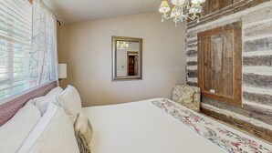 A bedroom with a bed, a chandelier, a mirror, and a wooden wall. - Dog-friendly Suite With a Fireplace - 290 Wine Tasting Trail (Fredericksburg)