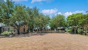 A spacious outdoor area with a dirt ground, surrounded by trees and a stone building with a small entrance. - Dog-friendly Suite With a Fireplace - 290 Wine Tasting Trail (Fredericksburg)