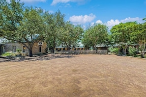 A spacious outdoor area with a dirt ground, surrounded by trees and a stone building with a small entrance. - Dog-friendly Suite With a Fireplace - 290 Wine Tasting Trail (Fredericksburg)
