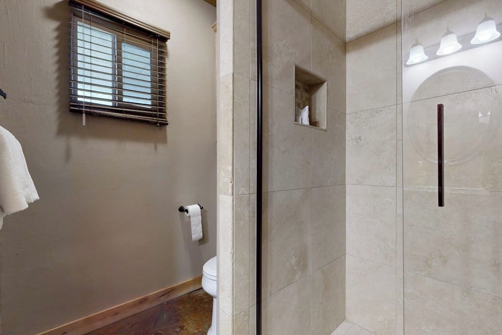 Un baño con inodoro, toallero, ventana con persianas y zona de ducha con puerta de cristal.