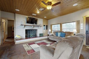 A living room with a fireplace, a ceiling fan, and a large window. - Renovated Waterfront Home With Wifi, Lake Views, Dock & Boat Lift - Dogs OK (Burnet)