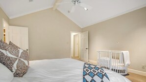 A bedroom with a bed, a crib, a ceiling fan, and a door leading to another room. - Inviting Waterfront Home With Pool, Patio, Fireplace, W/d, & Dog-friendly (Hunt)