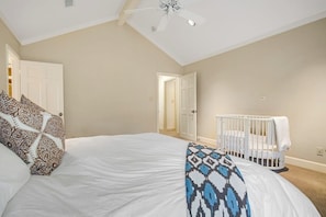 Un dormitorio con una cama, una cuna, un ventilador de techo y una puerta que da a otra habitación.