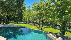 A swimming pool with a stone border, surrounded by trees and a grassy area. - Inviting Waterfront Home With Pool, Patio, Fireplace, W/d, & Dog-friendly (Hunt)