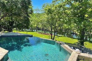 Una piscina con borde de piedra, rodeada de árboles y césped.