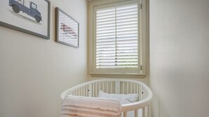 A white crib with a striped blanket, a window with blinds, and two framed pictures on the wall. - Inviting Waterfront Home With Pool, Patio, Fireplace, W/d, & Dog-friendly (Hunt)