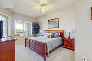 A bedroom with a wooden bed, bedside tables, a ceiling fan, a large window, and a mirror on the wall. - Dog-friendly & Spacious Condo With Lake Views, Large Balcony, & Pool (Horseshoe Bay)
