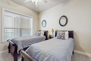 A bedroom with two beds, a ceiling fan, a window with blinds, and two wall mirrors. - Dog-friendly & Spacious Condo With Lake Views, Large Balcony, & Pool (Horseshoe Bay)