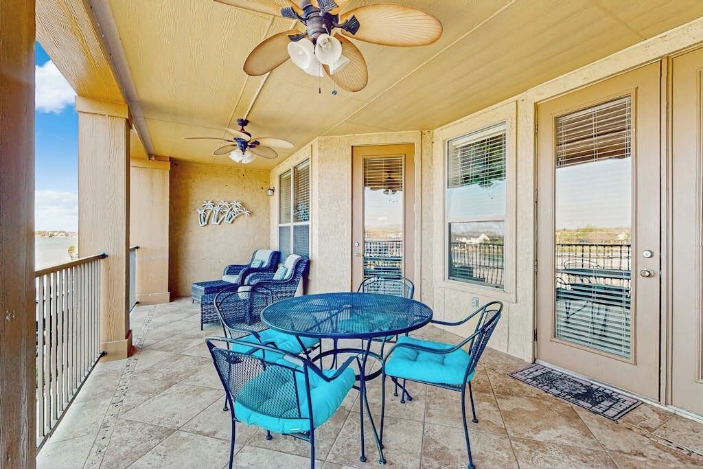 A covered patio with a round table and chairs, ceiling fans, and a view through the glass doors.