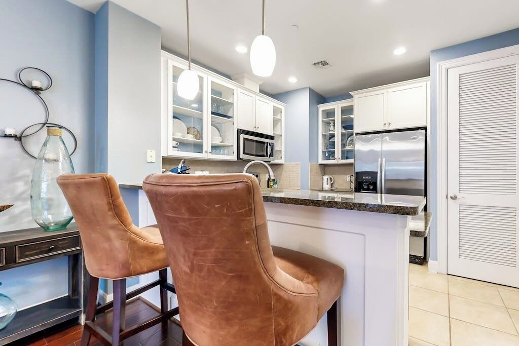 A kitchen with white cabinets, a stainless steel refrigerator, and two brown leather bar stools.