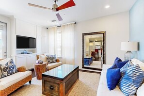 A modern living room with a flat-screen TV, a ceiling fan, a large mirror, and a sofa with patterned cushions. - Water-view Condo With Balcony, Smart Tvs, Washer/dryer and Pool (Horseshoe Bay)
