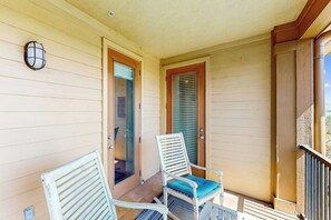 A balcony with two white chairs, one with a blue cushion, and a door with a glass panel. - Water-view Condo With Balcony, Smart Tvs, Washer/dryer and Pool (Horseshoe Bay)