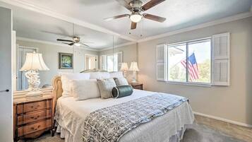 Une chambre à coucher avec un lit, des tables de chevet, des lampes, un ventilateur de plafond et une fenêtre ornée d’un drapeau américain.
