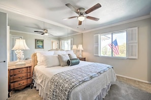 A bedroom with a bed, nightstands, lamps, a ceiling fan, and a window with an American flag. - Snowbird-friendly House With Game Room, Full Kitchen, Balcony & W/D (Kerrville)