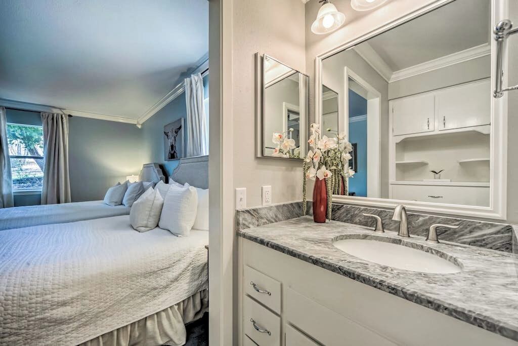 Quarto com cama grande, banheiro com pia de mármore e espelhos duplos, e um vaso de flores.