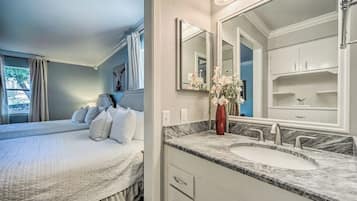 Quarto com cama grande, banheiro com pia de mármore e espelhos duplos, e um vaso de flores.