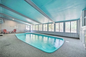 An indoor swimming pool with a blue ceiling, large windows, and a carpeted floor.