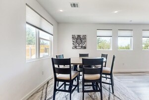 Un comedor con una mesa redonda y seis sillas, ventanas amplias y una obra de arte de un tigre en la pared.