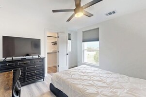 Un dormitorio con una cama, un televisor en una cómoda, un ventilador de techo y una ventana.