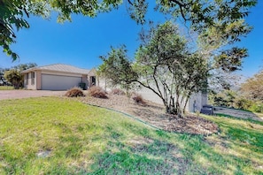 A residential property with a garage, a lawn, and a tree. - 2-story Home With Covered Patio, Balcony, Fireplace, Streaming, Great Views, W/D (Kerrville)