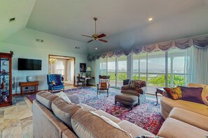 A spacious living room with a large window, a ceiling fan, and a variety of seating options. - 2-story Home With Covered Patio, Balcony, Fireplace, Streaming, Great Views, W/D (Kerrville)