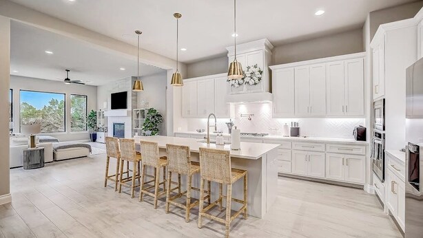 A modern kitchen with white cabinets, a central island with bar stools, pendant lighting, and a large window. - Exquisite Dog-friendly Home With Balcony, Enclosed Yard, Central AC, & W/D (Leander)