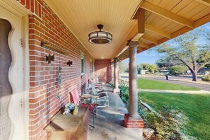 Eine überdachte Veranda mit Backsteinwand, Deckenventilator und Sitzgelegenheiten im Freien.