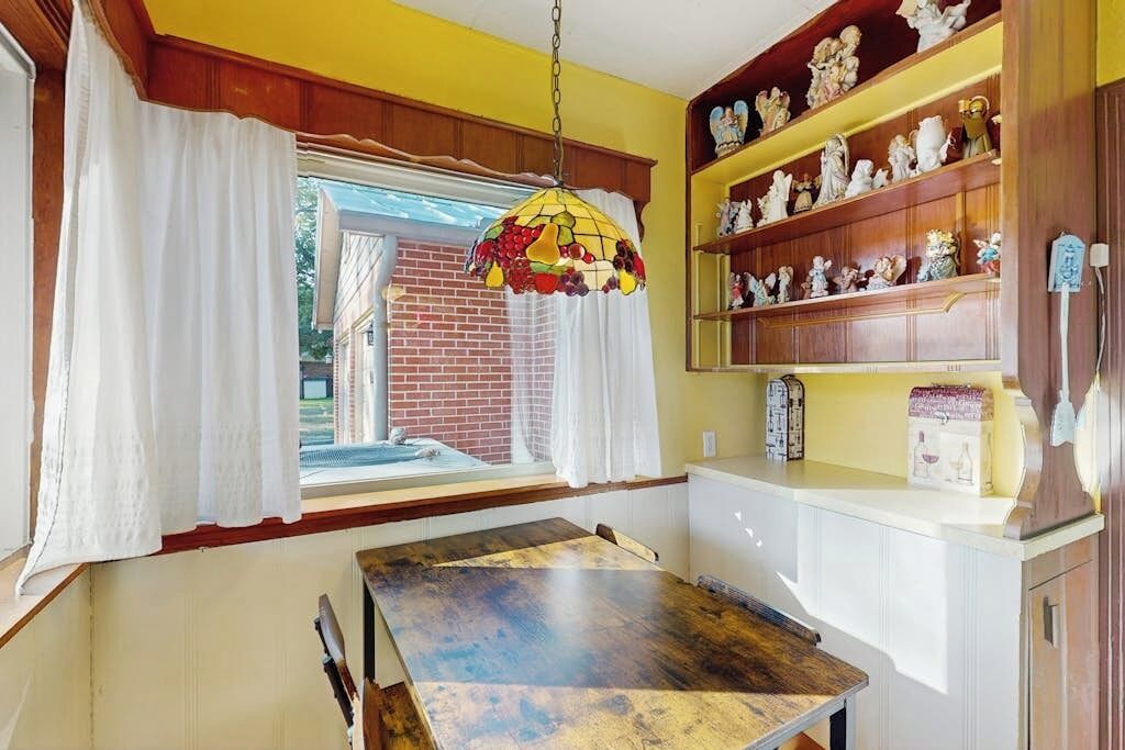A kitchen with a dining table, a hanging light fixture, and shelves with figurines.