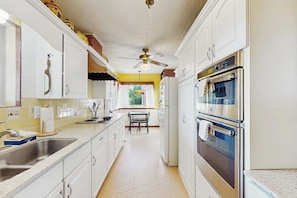 A kitchen with white cabinets, a stainless steel sink, a ceiling fan, and a window with a view of greenery. - Charming, Dog-friendly Home With Patio, Grill, & Parking - Close to Town (Fredericksburg)