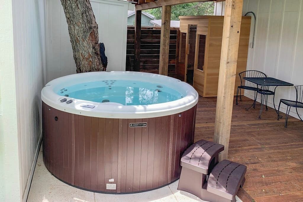 A hot tub with a wooden exterior, a wooden deck, and a small table with chairs.