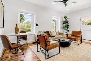 A modern living room with a round coffee table, leather armchairs, a sofa, and a large plant. - Historic Home a Block From Main St With Hot Tub, Sauna, Fast Wifi & Firepit (Fredericksburg)